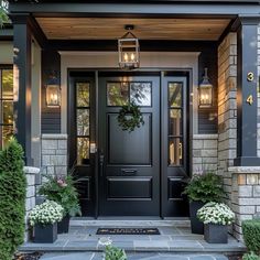 a black front door with two planters on each side and one light hanging above it