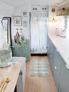 a small kitchen and dining area in a tiny home with wood floors, white curtains, and green cabinets