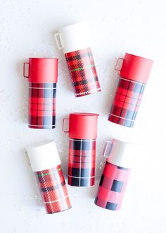 four red and black plaid coffee cups sitting next to each other on a white surface