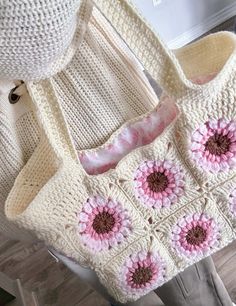 a crocheted purse with pink flowers on the front and bottom, sitting on a chair