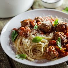 a white plate topped with spaghetti and meatballs next to a bowl of sauce on a wooden table