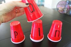 a hand is holding a red plastic cup with the letter i on it and five other cups in front of it