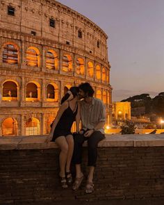 two people are sitting on a wall in front of the colossion at night