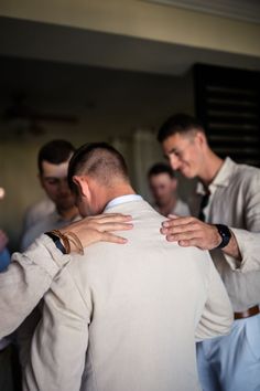 two men are hugging each other while another man is wearing a suit and white shirt