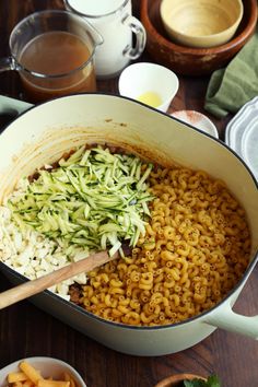 a pot filled with noodles and vegetables on top of a wooden table next to other dishes