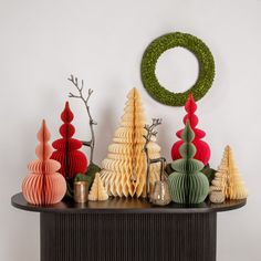 an assortment of paper christmas trees on a table with a green wreath above the top