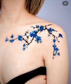 a woman's shoulder with blue flowers and leaves on the back of her body