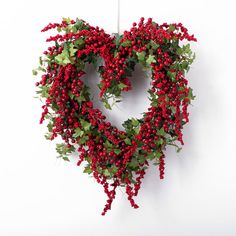 a heart shaped wreath with red berries and green leaves hanging on a white wall in the shape of a heart