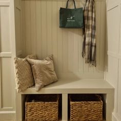 a white bench with two baskets under it and a coat rack on the wall next to it