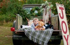 a young boy sitting in the back of an old truck with his teddy bear and christmas wreath