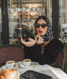 a woman sitting at a table taking a selfie with her cell phone while holding a cup of coffee