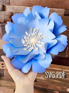 a person holding up a paper flower in front of a wooden background with the words svg df on it