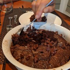 a person cutting into a chocolate cake in a white bowl on top of a table