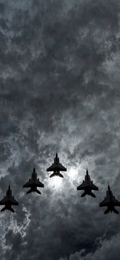 four fighter jets are flying in formation against a cloudy sky with the sun behind them