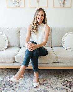 a woman sitting on top of a couch in front of a white couch with her legs crossed