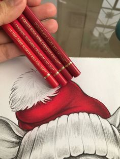 a hand holding three red pencils in front of a drawing of santa's hat