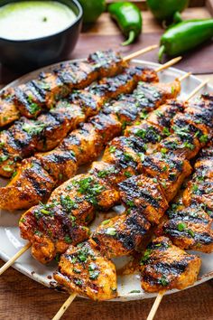 grilled chicken skewers on a white plate with green peppers and dipping sauce