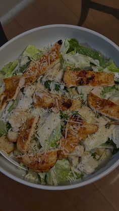 a salad with chicken and cheese in a white bowl on top of a wooden table