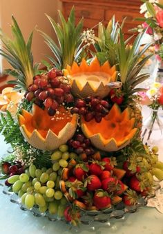 an arrangement of fruit on a table with flowers and greenery in the centerpiece