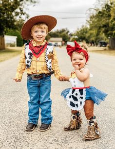 two children dressed up in costumes standing on the side of a dirt road holding hands