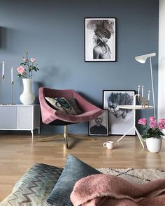 a living room with blue walls and pictures on the wall, pink chair in foreground