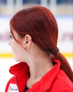 a woman with red hair is standing in front of an ice rink wearing a red jacket