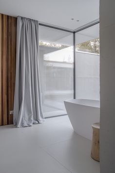 a white bath tub sitting under a window next to a wooden wall with curtains on it