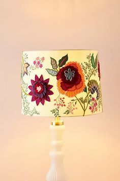 a lamp that is sitting on top of a white base with flowers painted on the lampshade