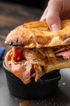 a person is holding a sandwich with meat and onions on it, in a black container