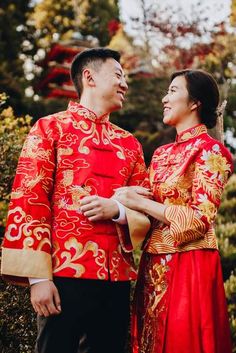 a man and woman in traditional chinese clothing standing close to each other with trees behind them