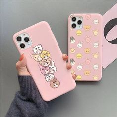 a person holding up two phone cases with cartoon characters on them, one is pink and the other is white