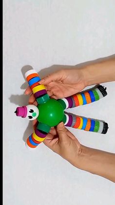 two hands are holding colorful toys on a white surface and one hand is holding a green ball