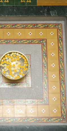 a bowl with yellow flowers in it sitting on a tiled floor