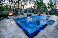 an outdoor swimming pool surrounded by stone steps and fire pit with lights on each side