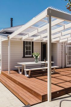 a white house with a wooden deck and picnic table in the foreground, under a pergolated roof