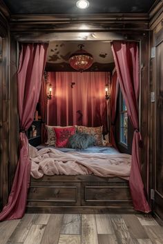 a bed with red drapes and pillows in a room that has wood flooring