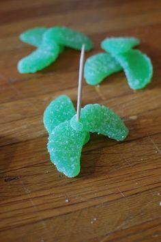 some green gummy bears on a wooden table with toothpicks sticking out of them