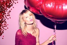 a woman in a pink dress holding two red balloons and blowing it with her tongue