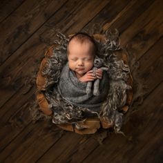 a newborn baby wrapped in grey and holding a teddy bear