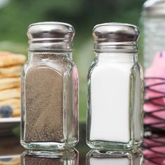 two salt and pepper shakers sitting on top of a table next to each other