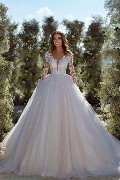 a woman wearing a wedding dress with long sleeves and lace on the top, standing in front of trees