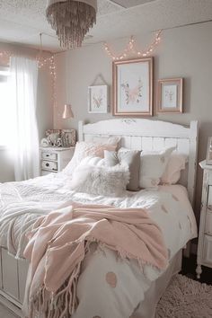 a white bed topped with pillows and blankets next to a window covered in pink lights