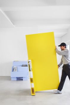 a man moving a large yellow piece of furniture in a room with white walls and floors