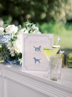 there is a card with a dog on it next to a drink glass and flowers