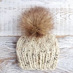 a white knit hat with a brown fur pom - pom on top of it