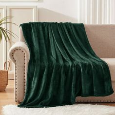 a couch with a green blanket on top of it next to a white rug and potted plant