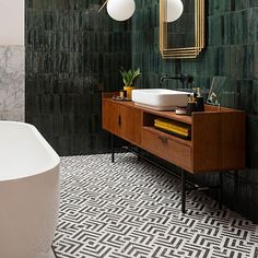 a white bath tub sitting next to a wooden cabinet in a bathroom with green tiles on the walls