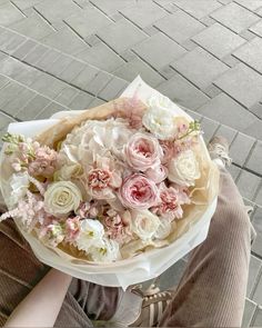 a woman holding a bouquet of flowers on her lap while sitting in front of a brick sidewalk