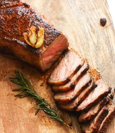 a piece of meat is sitting on a cutting board with some rosemary sprigs