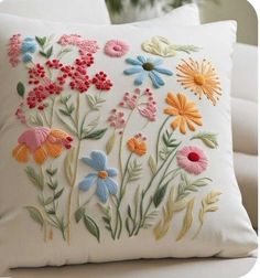 an embroidered pillow with colorful flowers on the front and back, sitting on a white couch